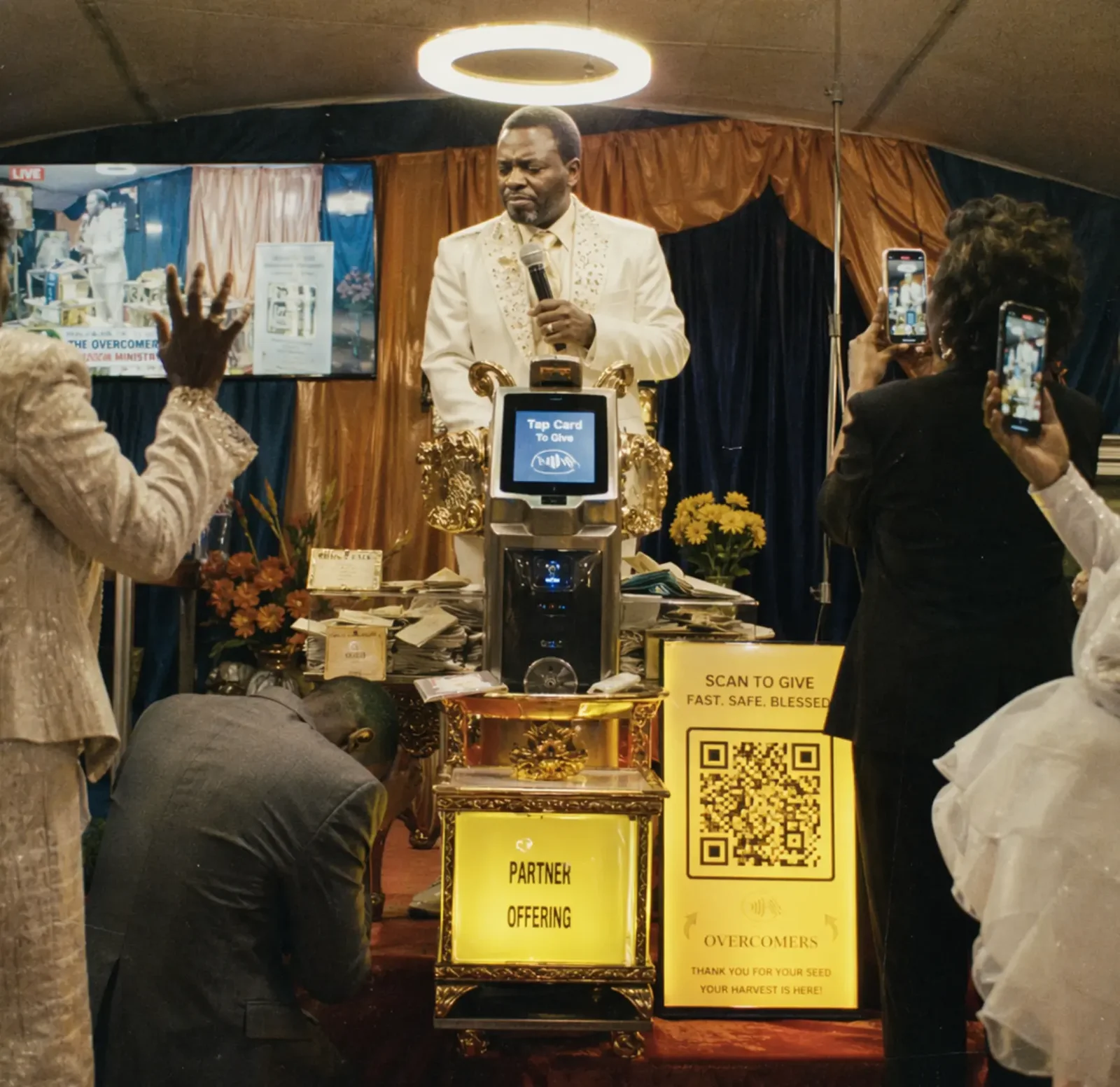 A preacher speaking from a pulpit with digital donation displays