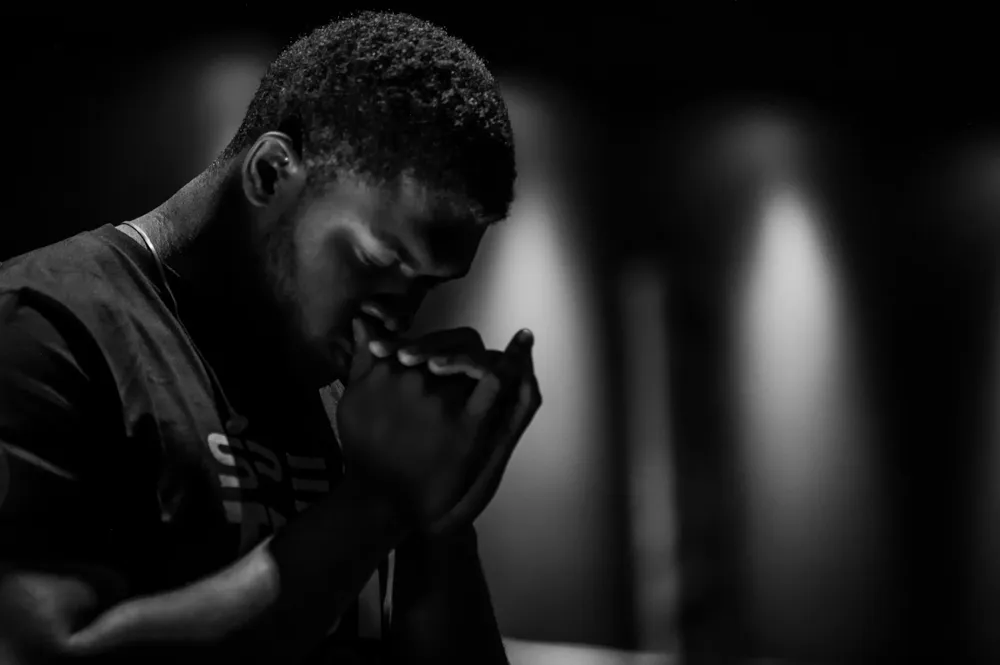 An athlete with head bowed into clasped hands in low light