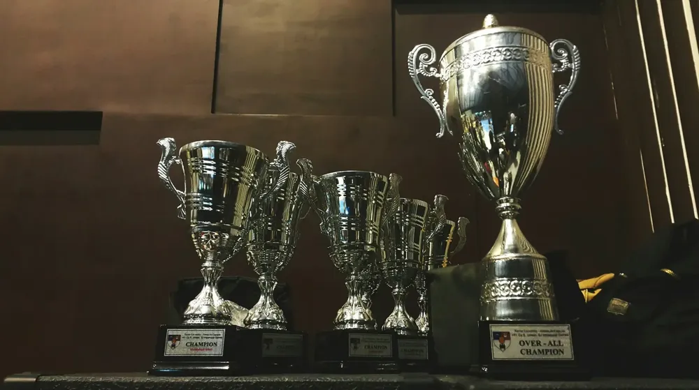 Silver trophies lined up on a dark shelf