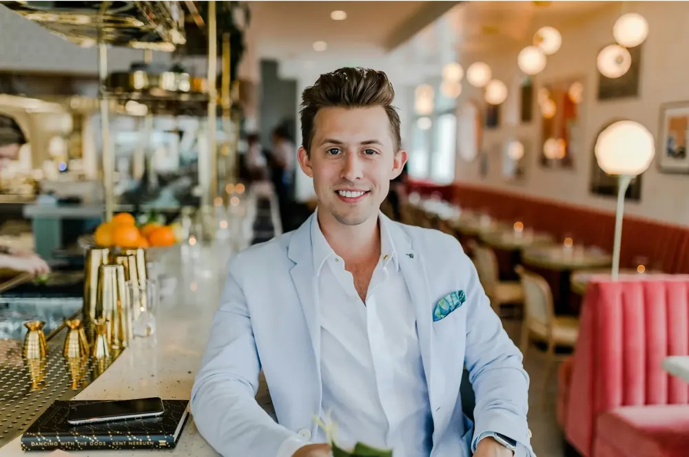 A smiling man in a pale blue suit seated in a restaurant